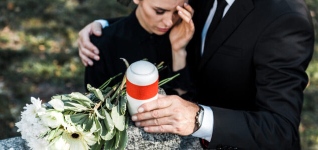 selective focus of flowers on tomb near senior man hugging upset woman
